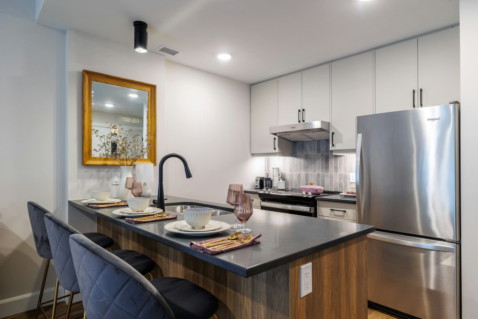 Сучасна біла кухня з багаторівневим освітленням: точкові стельові світильники, підсвітка фартуха та дзеркало для відбиття світла