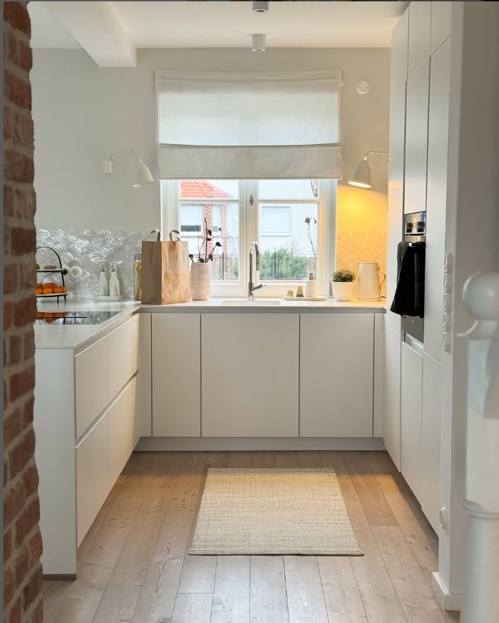 Біла мінімалістична кухня: білі римські штори на вікні та декоративна плитка-луска на фартуку