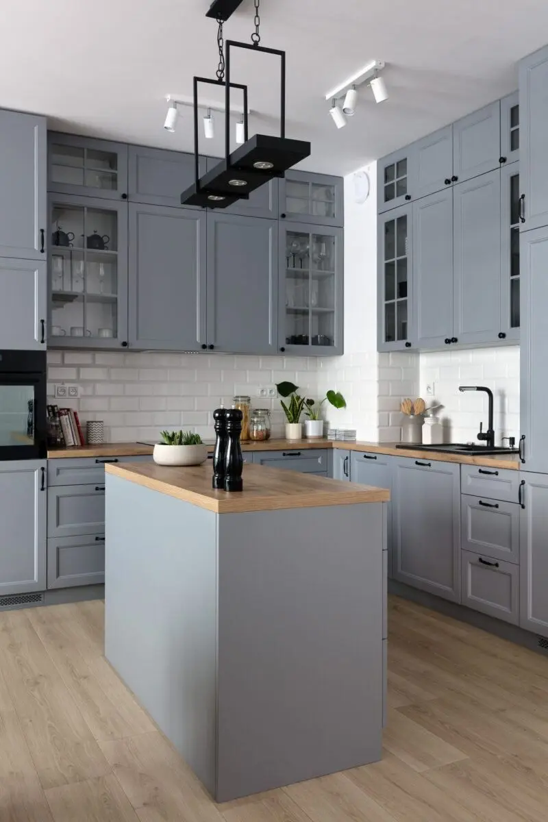 Світло-сіра кухня з класичними рамковими фасадами, світлою дерев'яною стільницею та контрастною чорною фурнітурою 