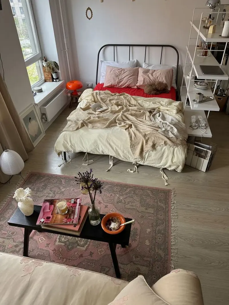 Велике ліжко з чорним металевим узголів’ям у просторій світлій спальні з відкритими полицями та акцентним чорним столиком