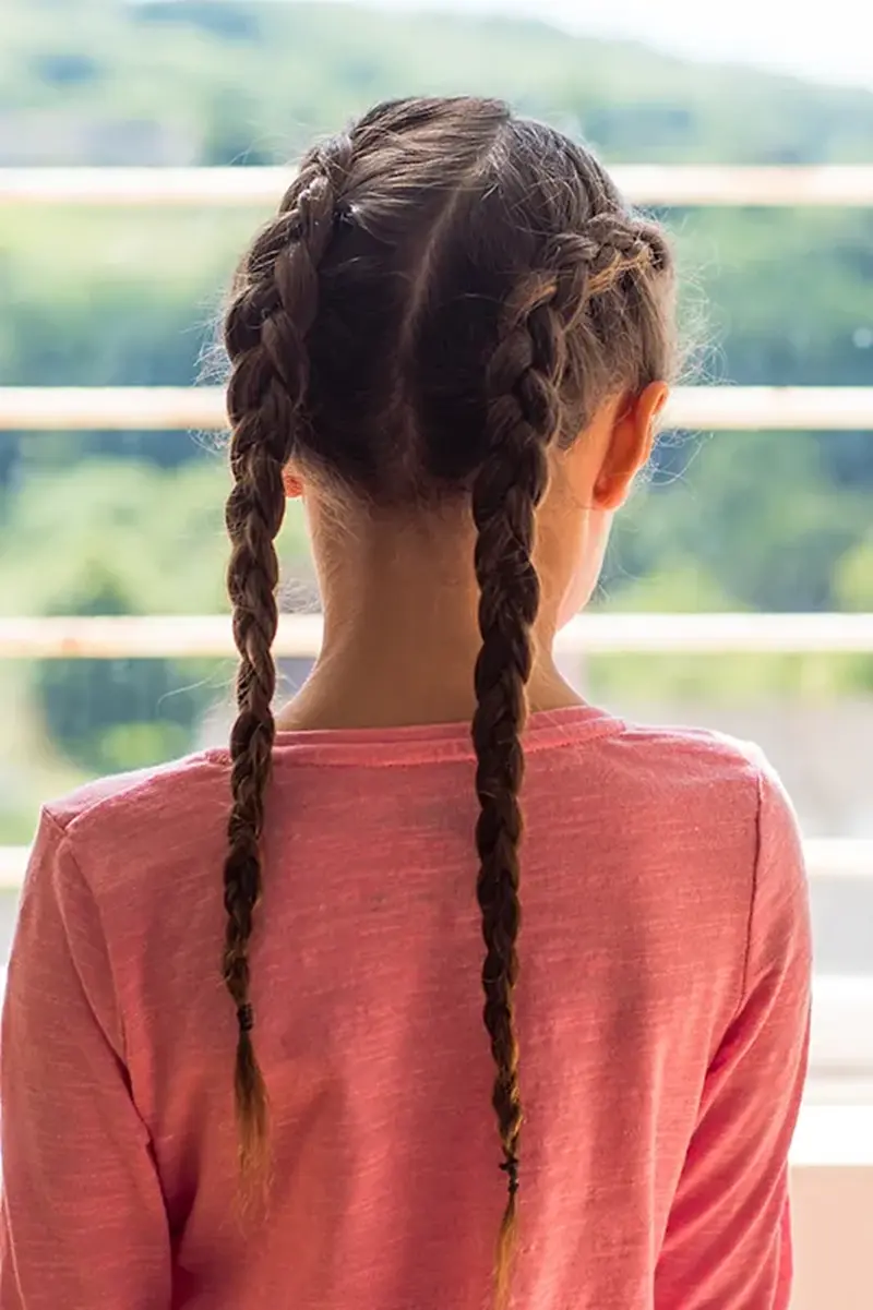 Дві голландські коси на довгому темному волоссі від самого чола до кінчиків на прямий проділ