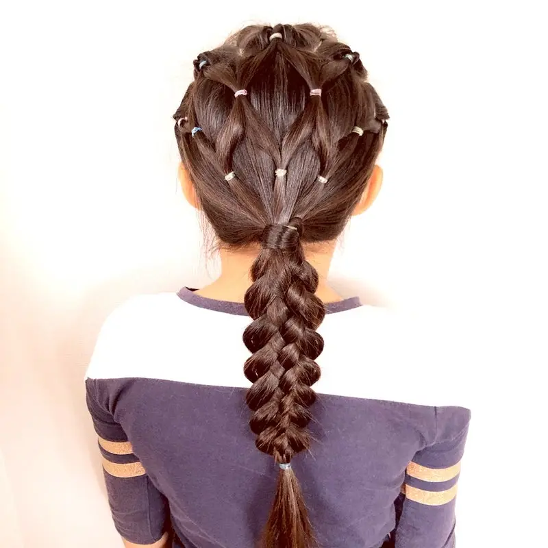 Зачіска з геометричною сіткою з хвостиків на маківці, яка плавно переходить у довгу щільну косу