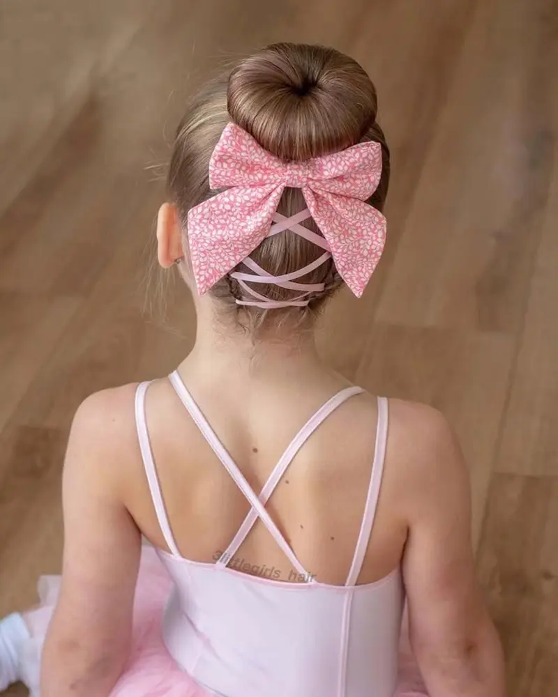 Тугий пучок балерини, прикрашений корсетним плетінням рожевою стрічкою по потилиці та бантом біля основи